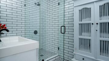 Un baño con azulejos blancos tipo metro, una cabina de ducha con mampara de vidrio y un mueble blanco con puerta.