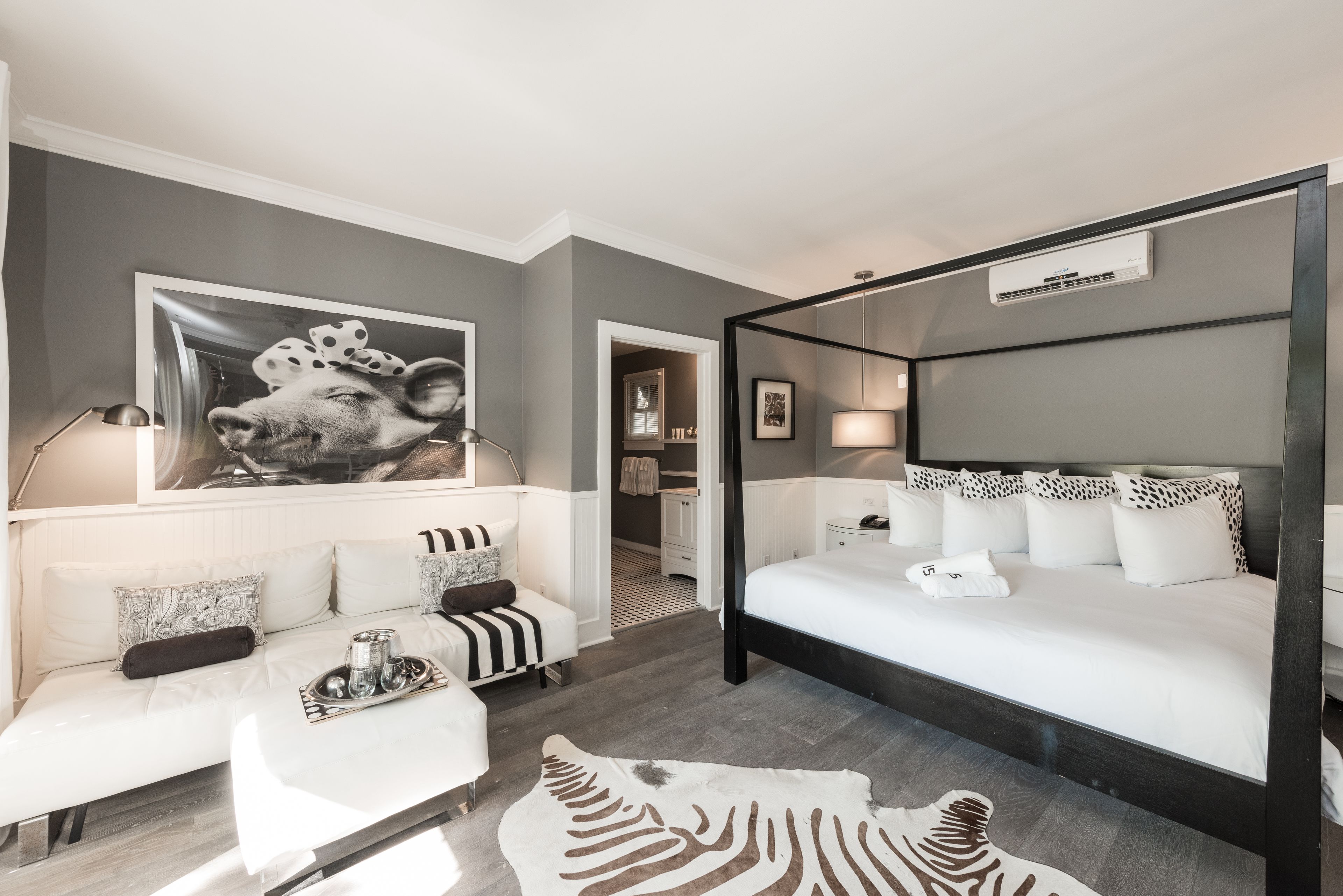 A modern hotel room with a large bed, a sofa, a zebra rug, and a wall-mounted air conditioning unit.