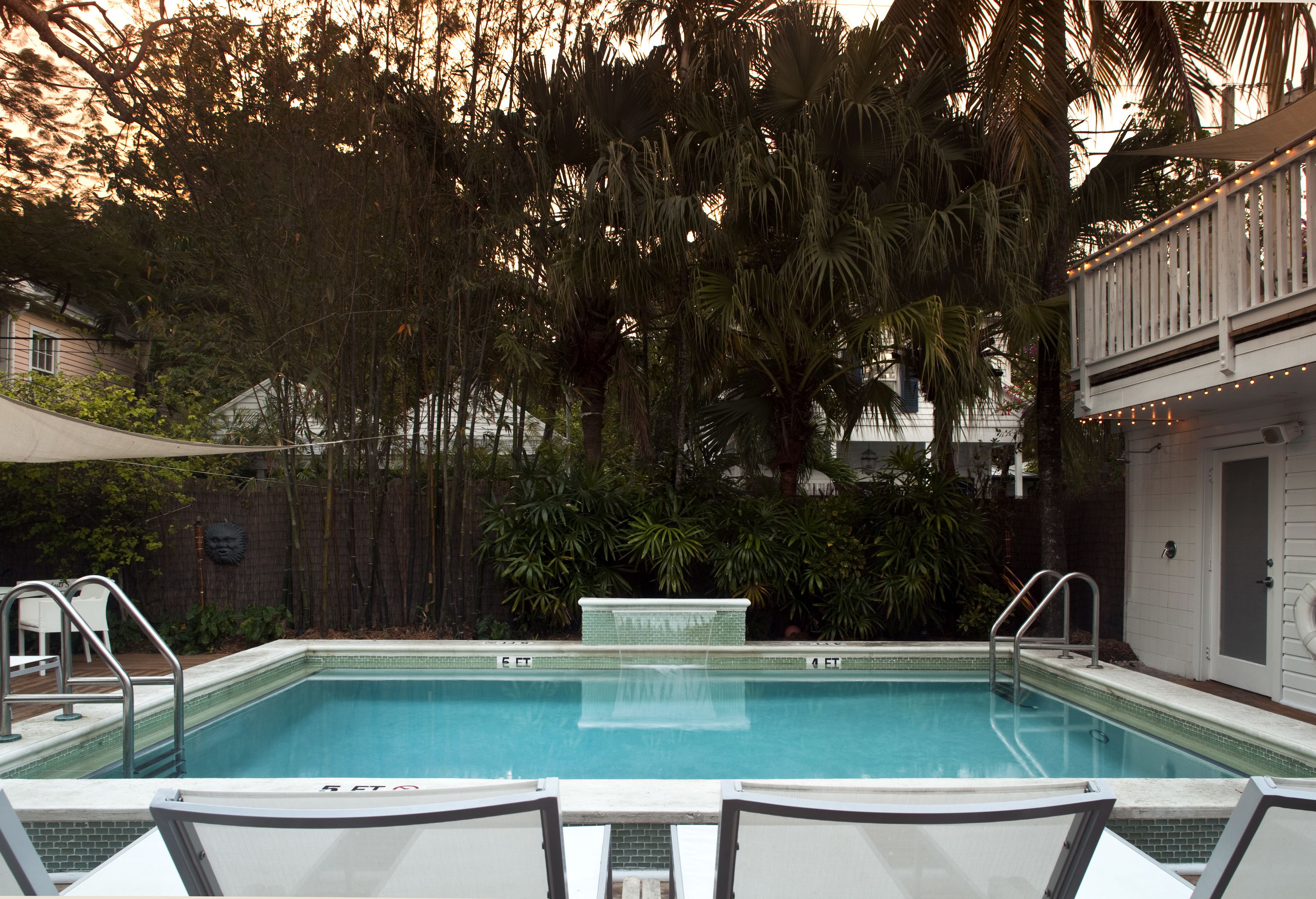 Une piscine rectangulaire bordée de carreaux, entourée de chaises longues et d’une terrasse en bois.