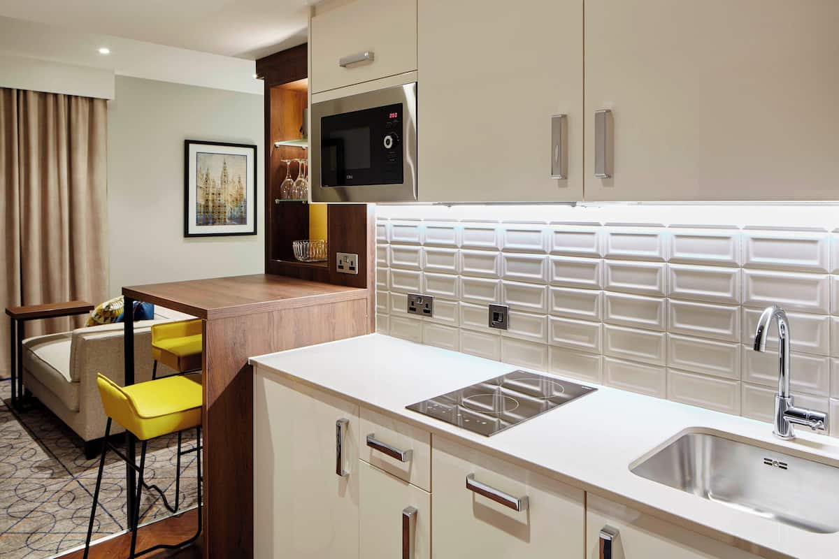 A compact hotel kitchen with a microwave, sink, and bar stools.