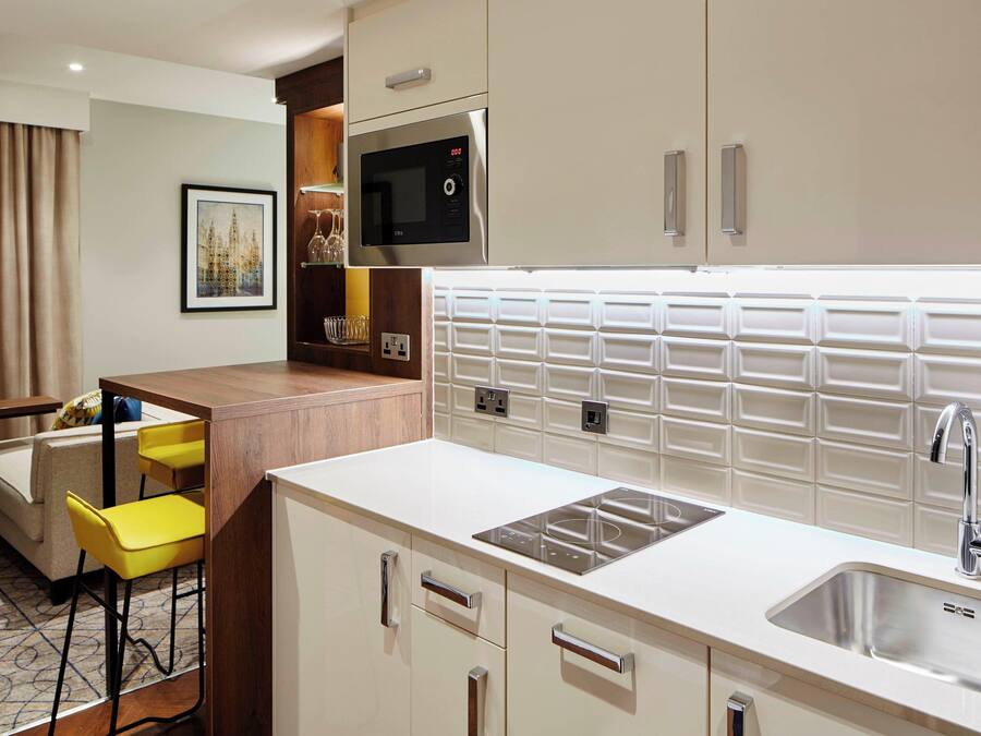 A compact hotel kitchen with a microwave, sink, and bar stools.