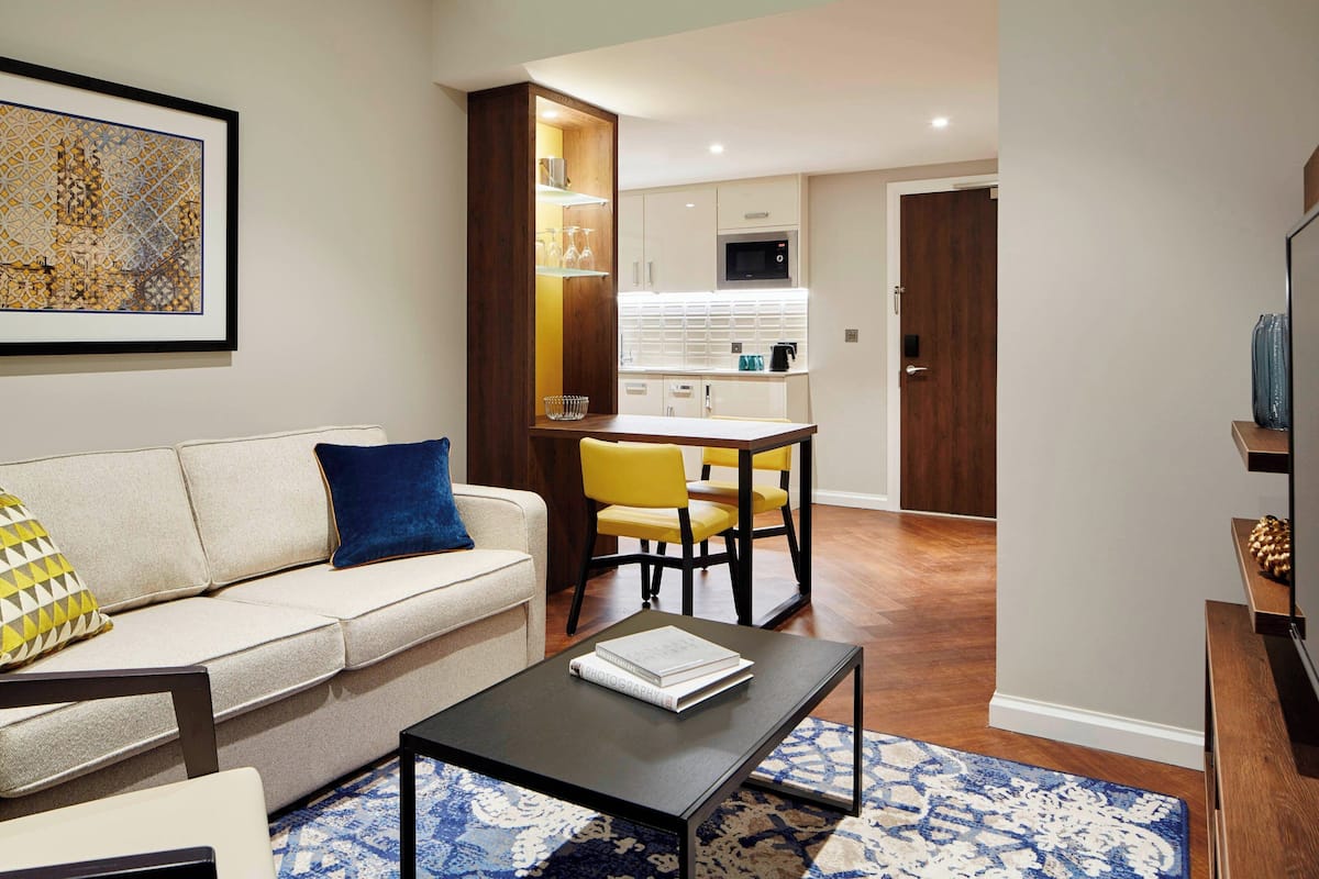 A modern living room with a sofa, a coffee table, and a dining area with yellow chairs.