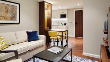 A modern living room with a sofa, a coffee table, and a dining area with yellow chairs.