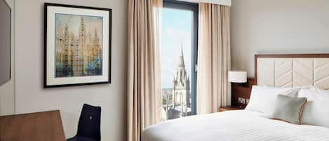 A hotel room with a large bed, a chair, a desk, and a framed picture on the wall.