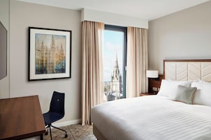Quarto de hotel com uma cama grande, uma cadeira, uma escrivaninha e um quadro na parede.