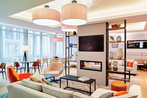 Um hall de hotel moderno com área de estar, TV na parede e estante com diversos objetos.