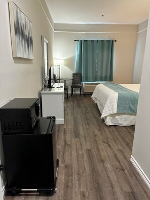 A compact hotel room with a bed, a desk with a computer, a chair, a small table, and a microwave. - Deluxe 6 Inn & Suites (Los Fresnos)