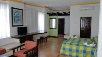 Um quarto com cama, escrivaninha, cadeira e televisão.