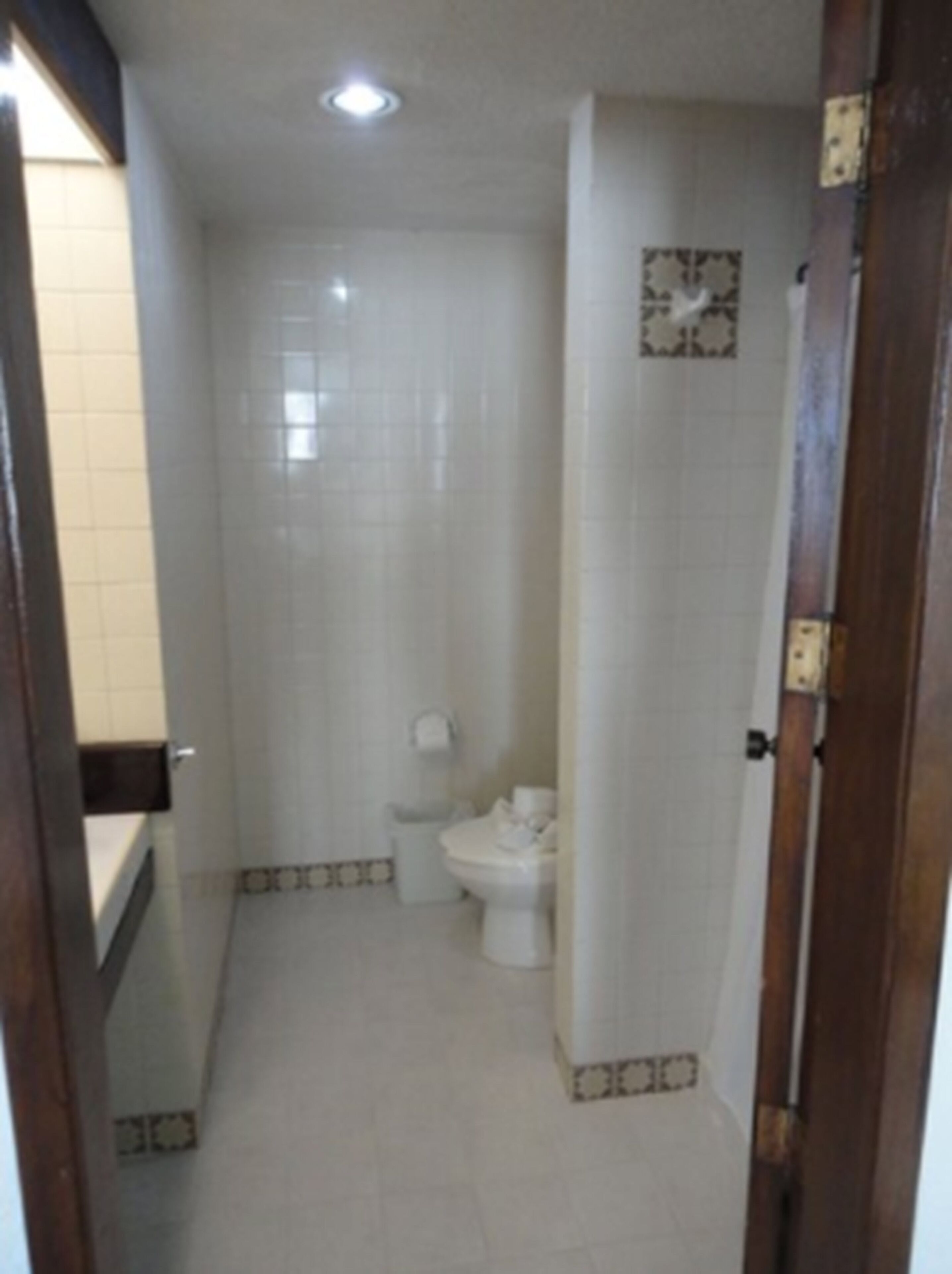 A small, narrow bathroom with white tiles, a toilet, and a sink.