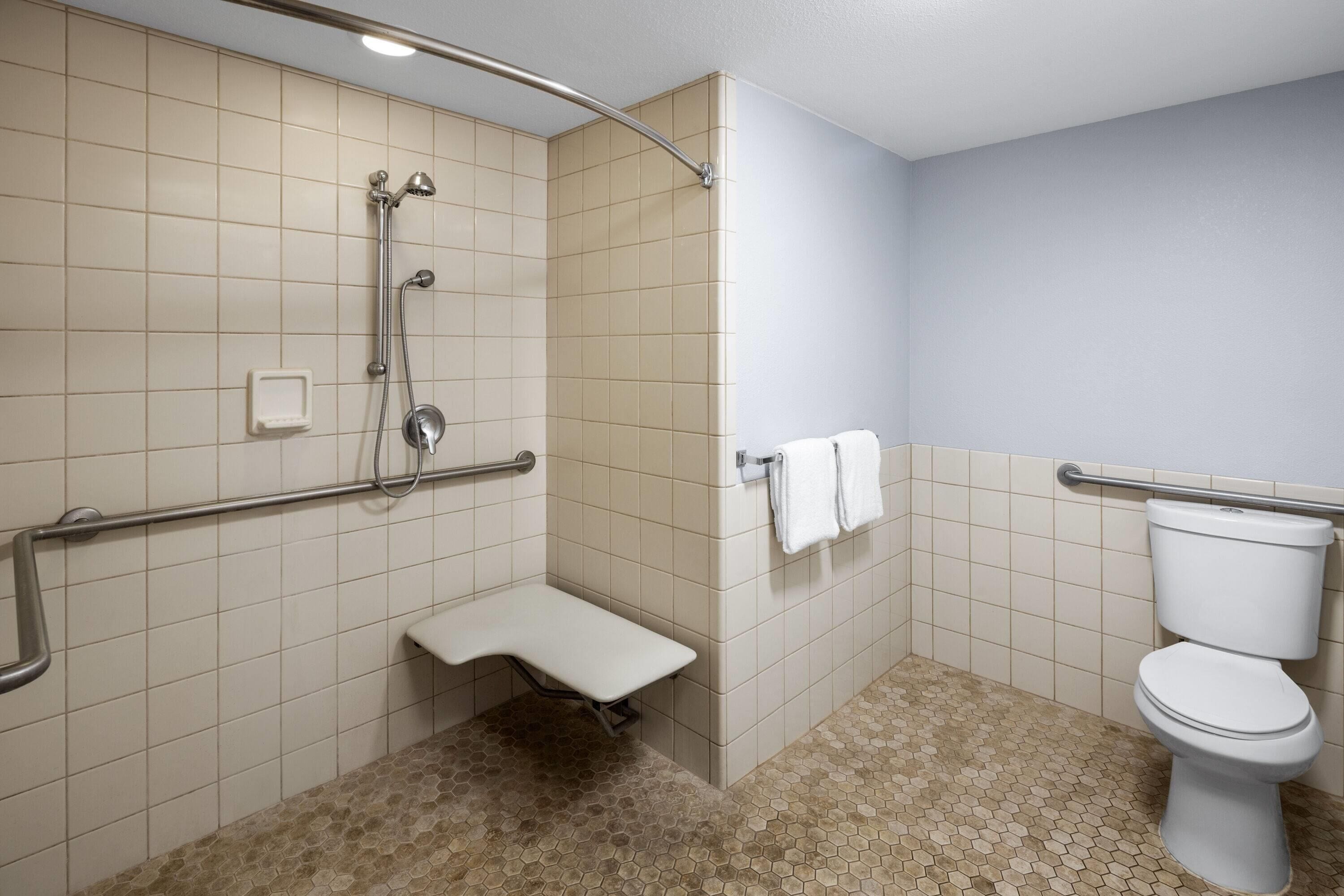 Un baño con ducha, inodoro y un banco.