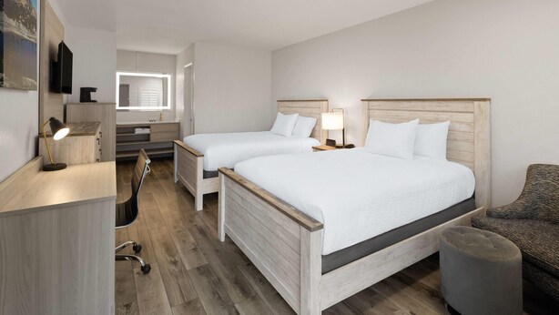 Quarto de hotel com duas camas, uma mesa, uma cadeira e um pequeno banquinho.