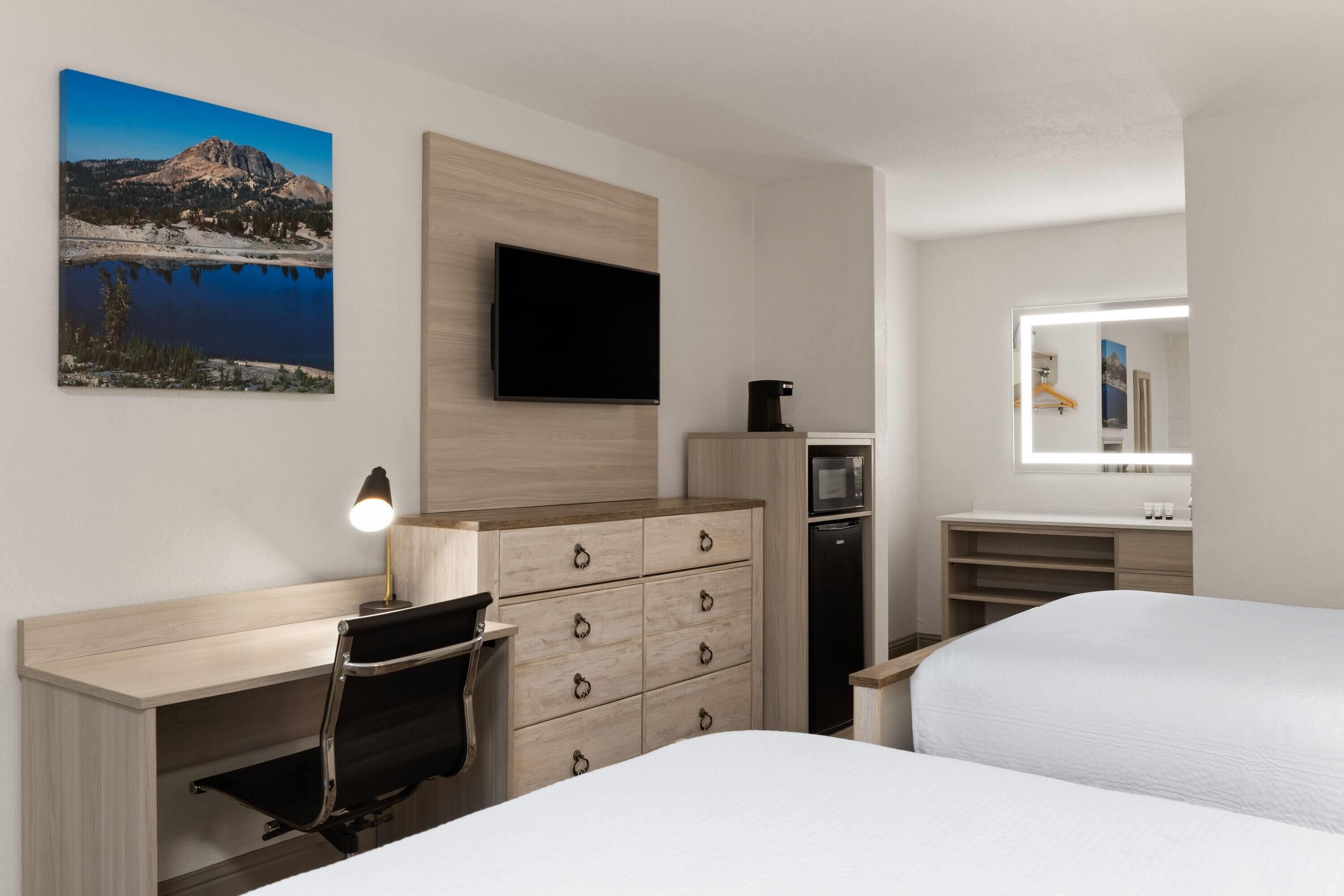 Ein Hotelzimmer mit Bett, Schreibtisch mit Stuhl, Kommode, Fernseher, Kaffeemaschine, Mikrowelle und Spiegel im Badezimmer.