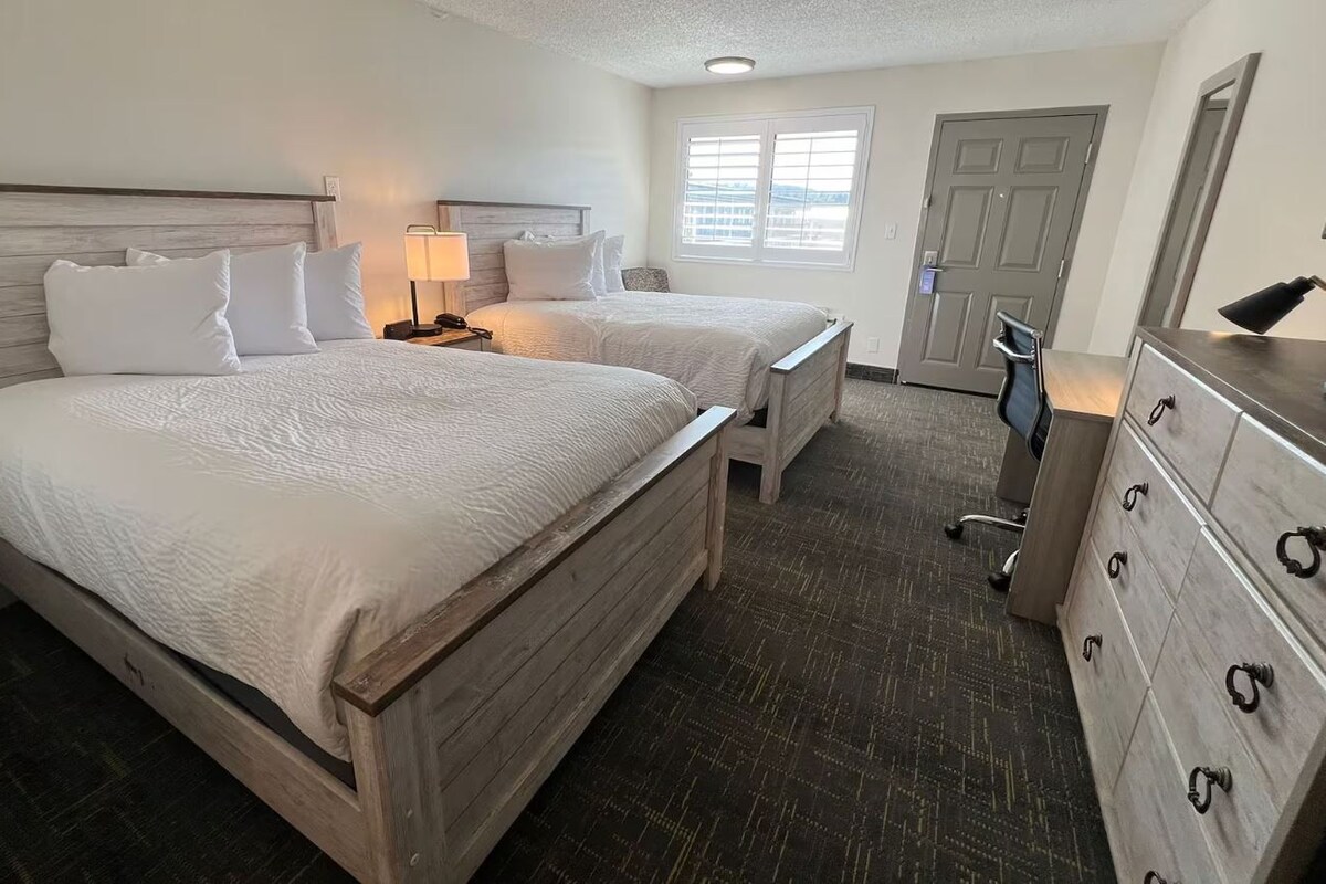 A hotel room with two beds, a dresser, a desk with a lamp, and a chair.