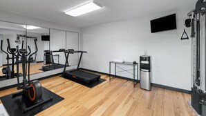 Academia moderna com equipamentos de exercícios, bebedouro e um espelho grande.