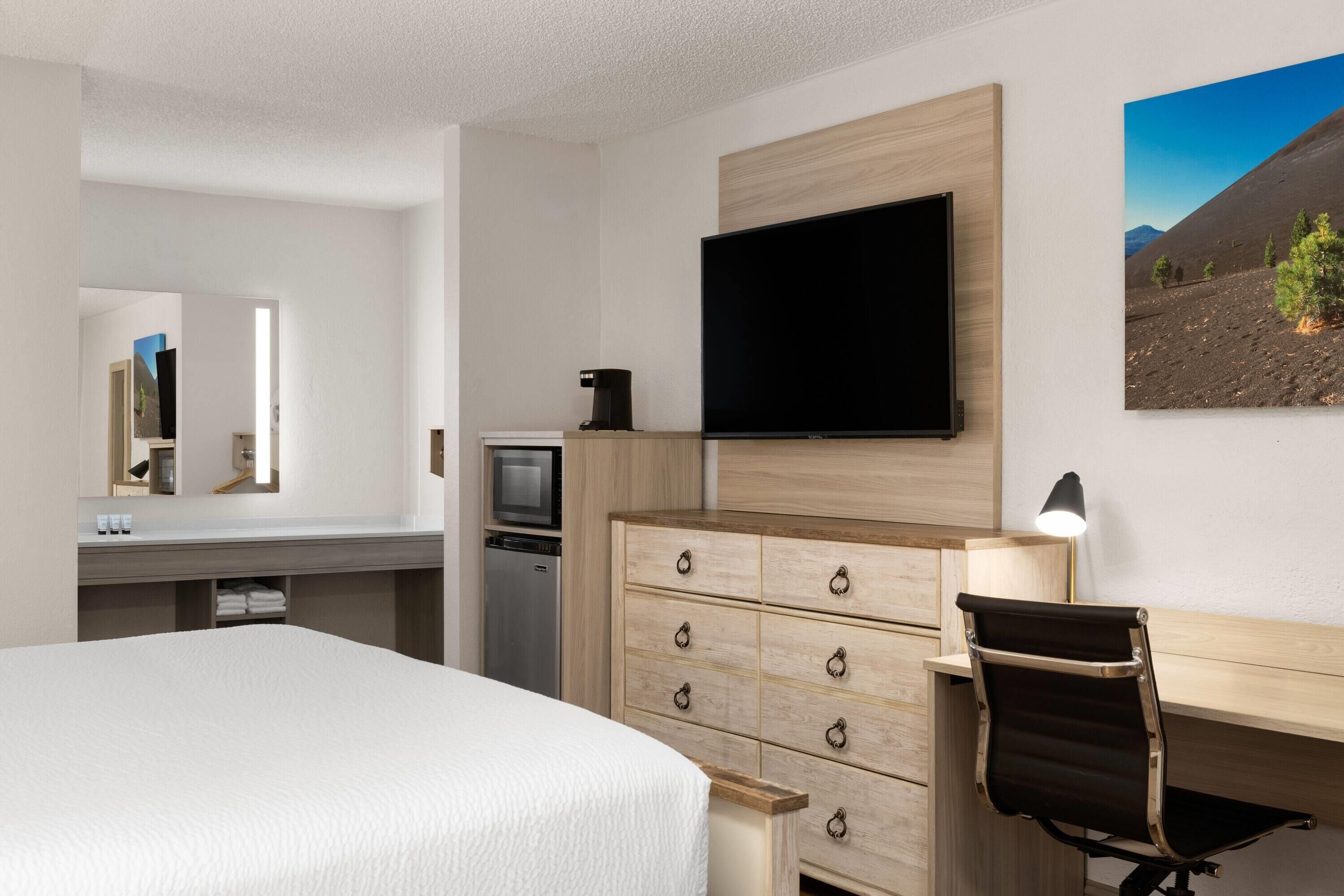 Una habitación de hotel con cama, escritorio con silla, televisor, cómoda y un cuadro en la pared.