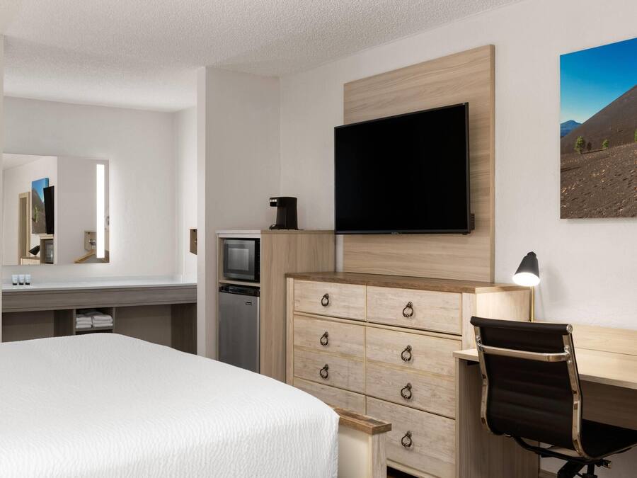 Una habitación de hotel con cama, escritorio con silla, televisor, cómoda y un cuadro en la pared.