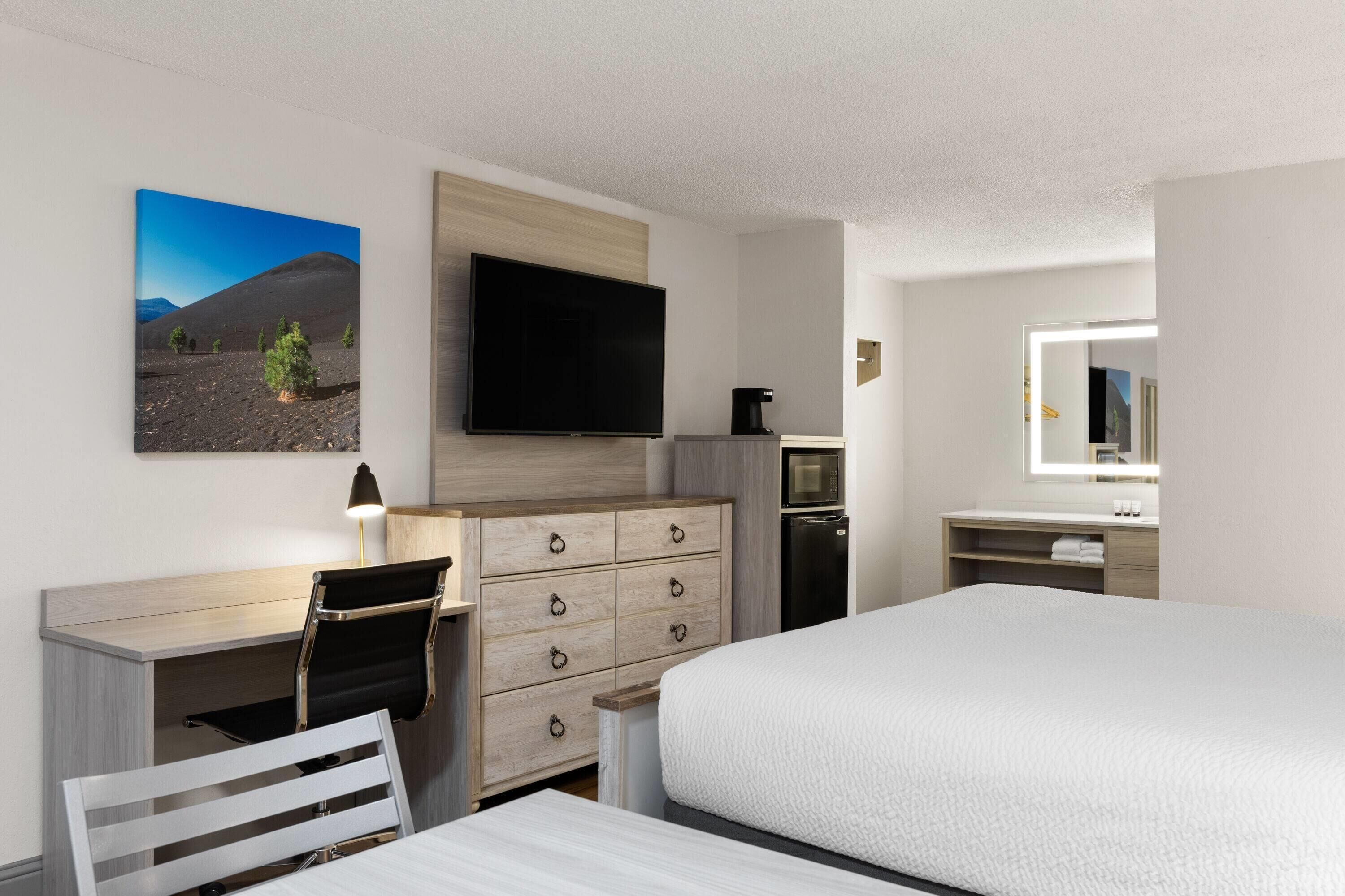 A hotel room with a bed, a desk with a chair, a dresser, a television, a coffee maker, and a mirror.