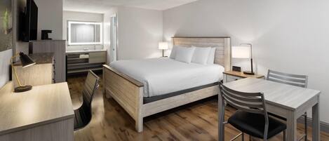 A modern hotel room with a wooden bed, a desk, a chair, a small table, and a TV.