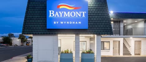 A motel named Baymont by Wyndham with a blue sign, a covered entrance, and two planters with flowers.