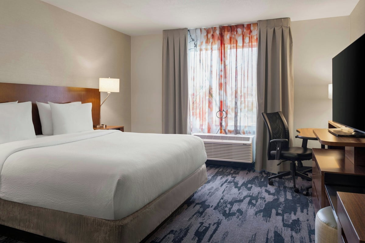 A hotel room with a large bed, a desk, a chair, a TV, and a window with curtains.