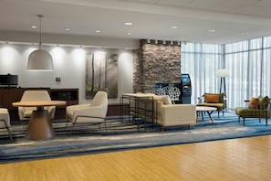 A modern hotel lobby with a stone fireplace, a round dining table, and comfortable seating. - Fairfield Inn & Suites by Marriott Indianapolis Fishers (Indianapolis)
