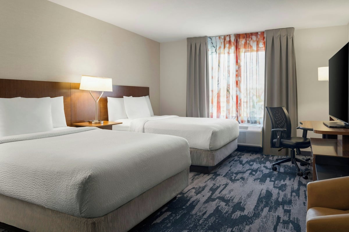 A hotel room with two beds, a desk, a chair, a TV, and a window with curtains.
