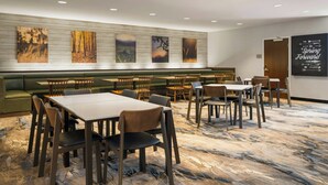 A hotel dining area with multiple tables and chairs, a green sofa, and wall art. - Fairfield Inn & Suites by Marriott Indianapolis Fishers (Indianapolis)