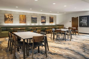 A hotel dining area with multiple tables and chairs, a green sofa, and wall art. - Fairfield Inn & Suites by Marriott Indianapolis Fishers (Indianapolis)
