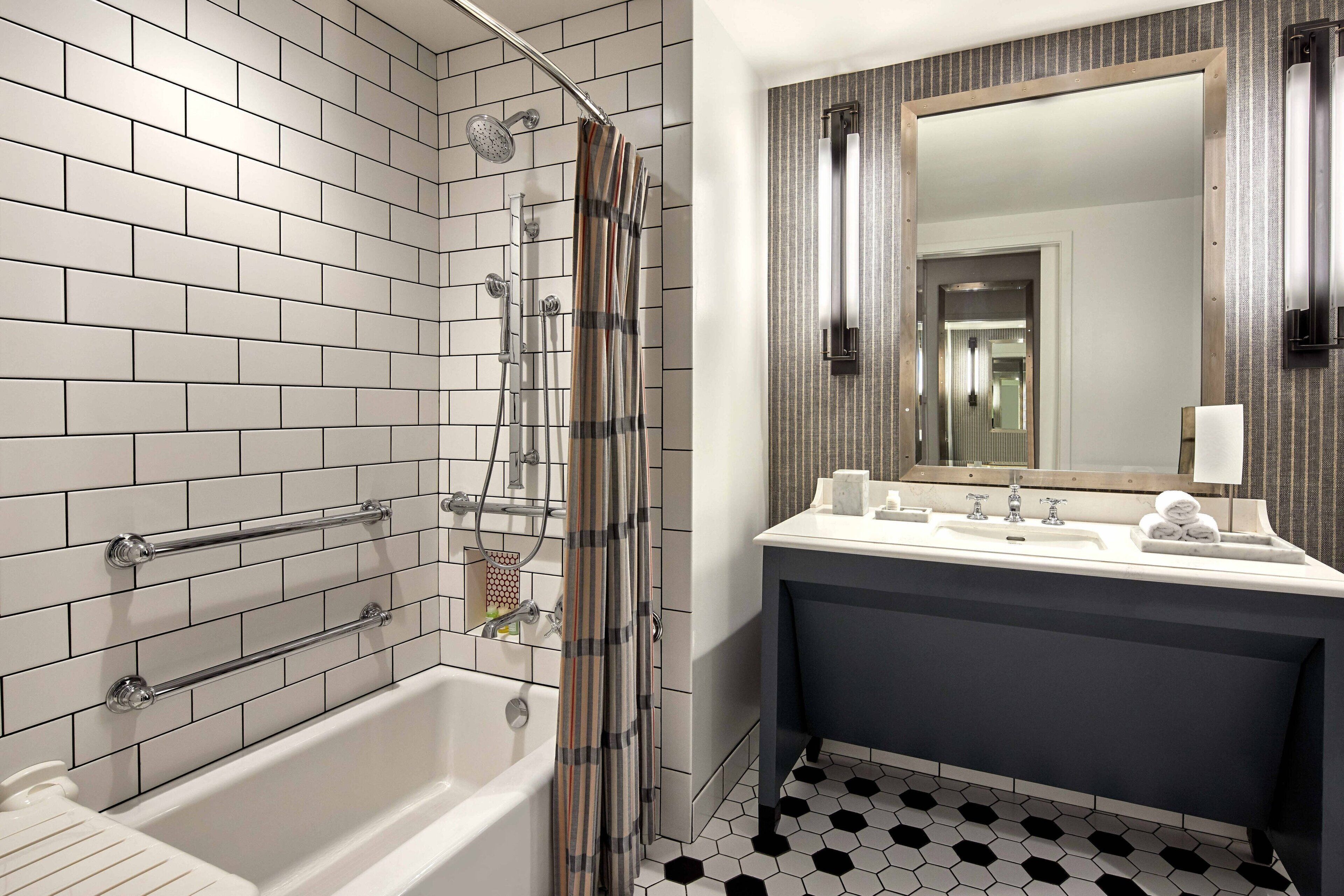 A modern bathroom with a white-tiled shower, a bathtub, a dark vanity with a mirror, and a black and white hexagonal tile floor.