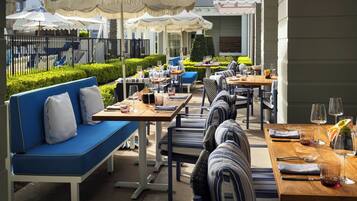 An outdoor dining area with tables and chairs, umbrellas, and a pool in the background.