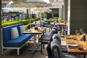 Un espace extérieur aménagé pour les repas, avec des tables et des chaises, des parasols, et une piscine en arrière-plan.