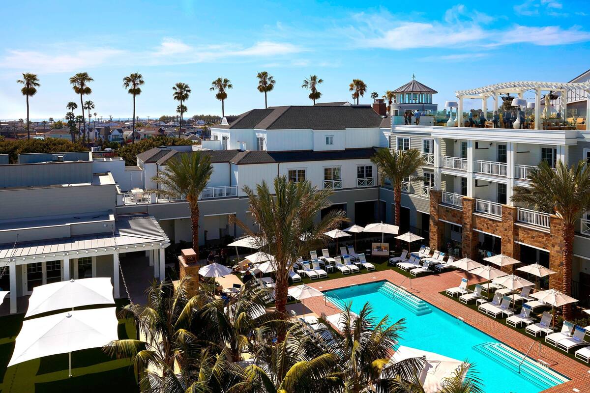 A pool area with lounge chairs and umbrellas, surrounded by palm trees and a building with a white facade.
