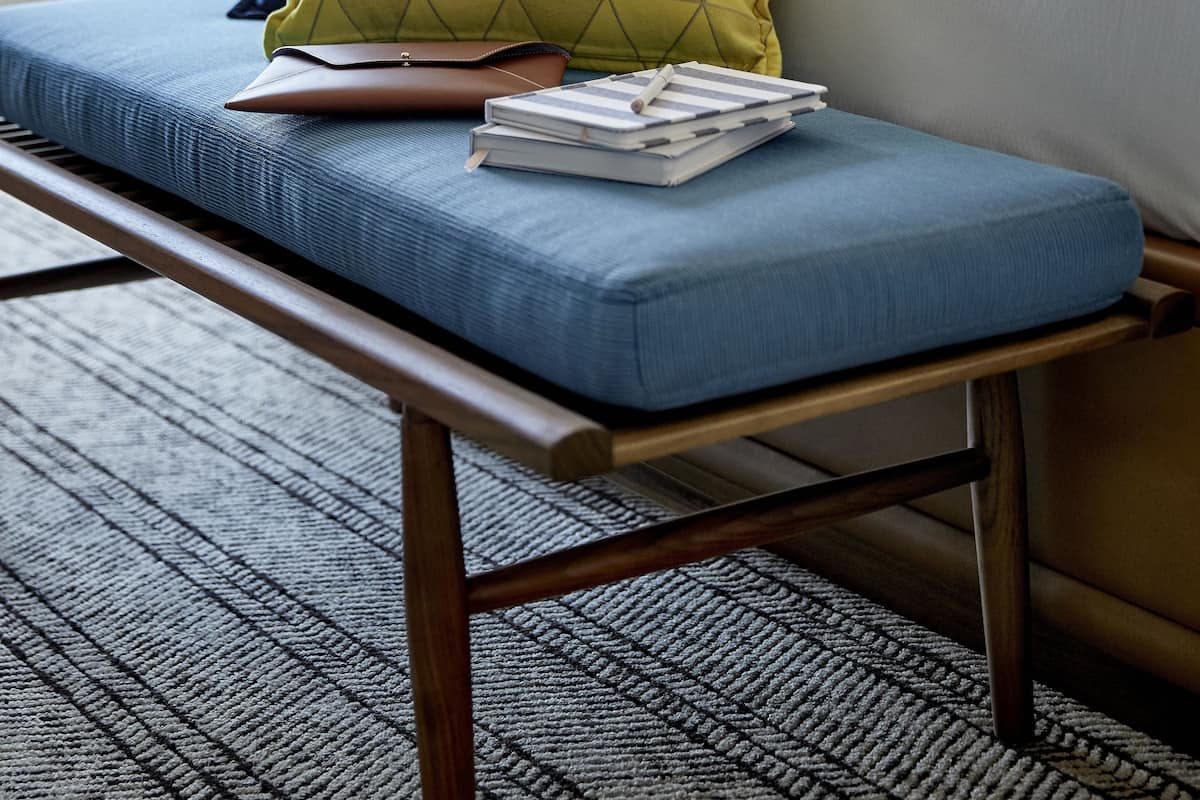 A hotel room with a bed, a blue sofa with cushions, a wooden bench, and a patterned carpet.