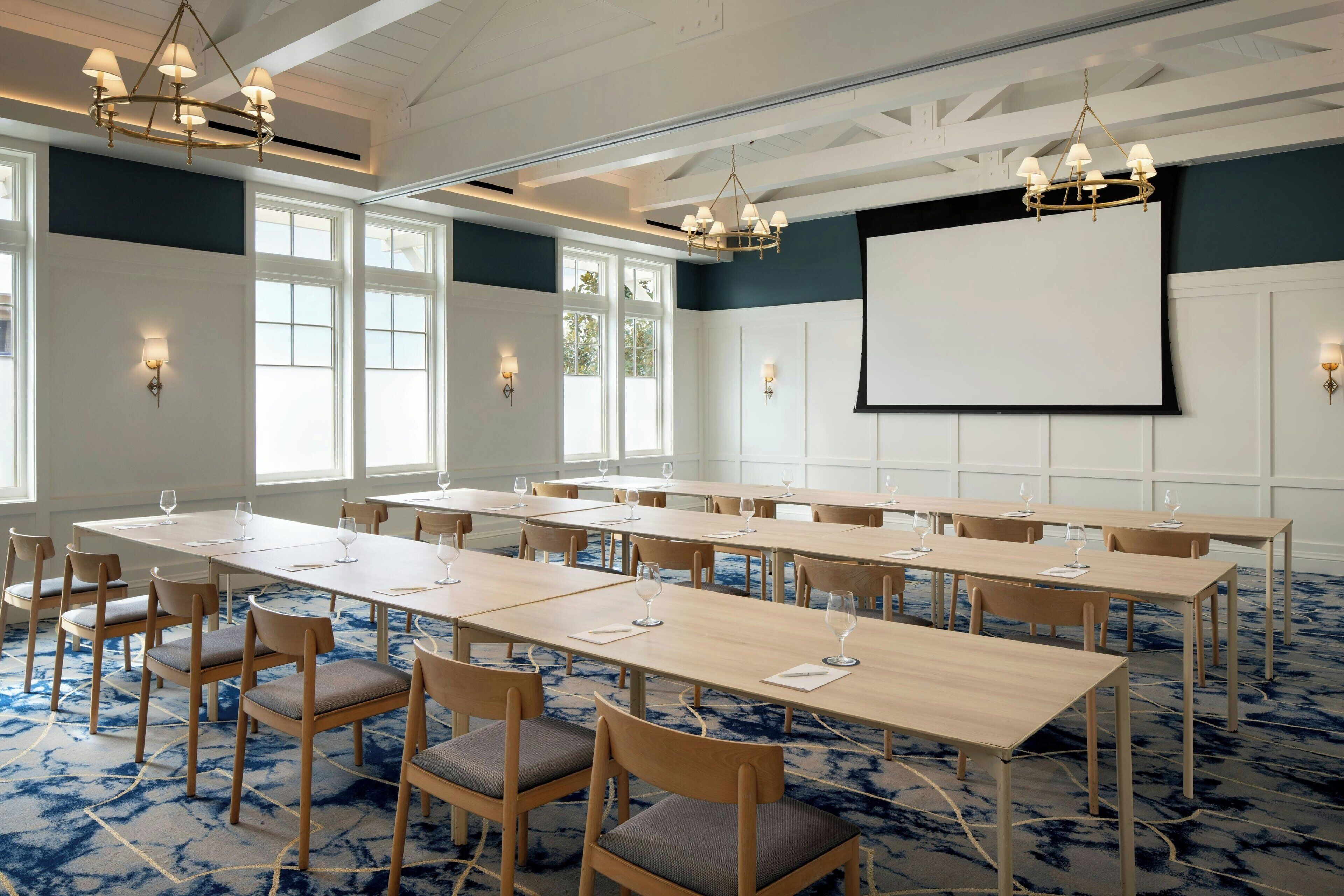 A conference room with long tables, chairs, and a projector screen.