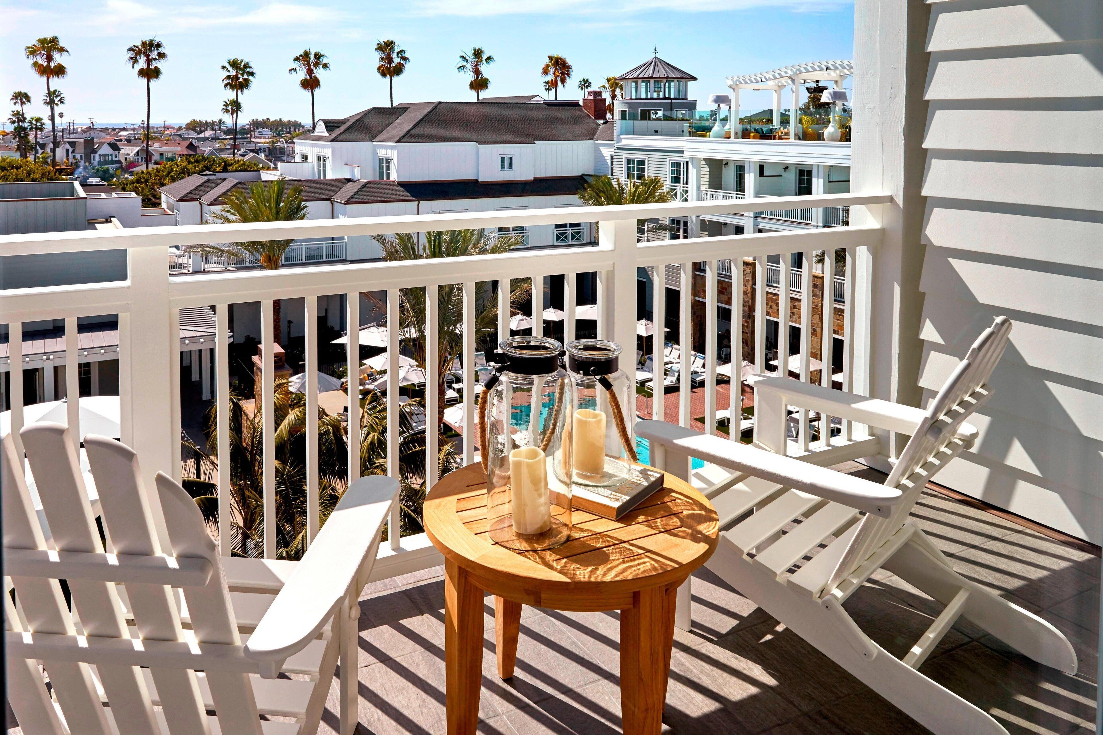 A balcony with white chairs, a wooden table with candles, and a view of palm trees and buildings.
