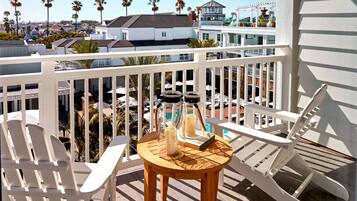 A balcony with white chairs, a wooden table with candles, and a view of palm trees and buildings.