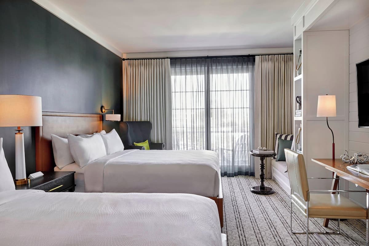 A hotel room with two beds, a desk, a chair, a TV, and a window with curtains.