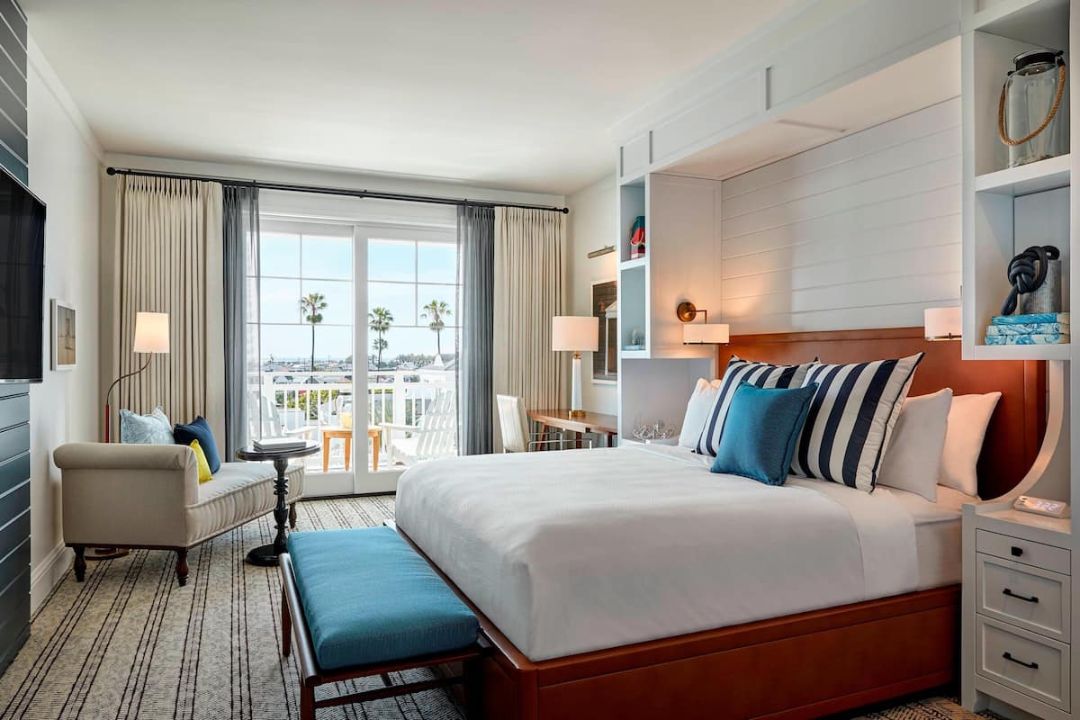 A hotel room with a large bed, a sofa, a desk, and a view of palm trees through the window.