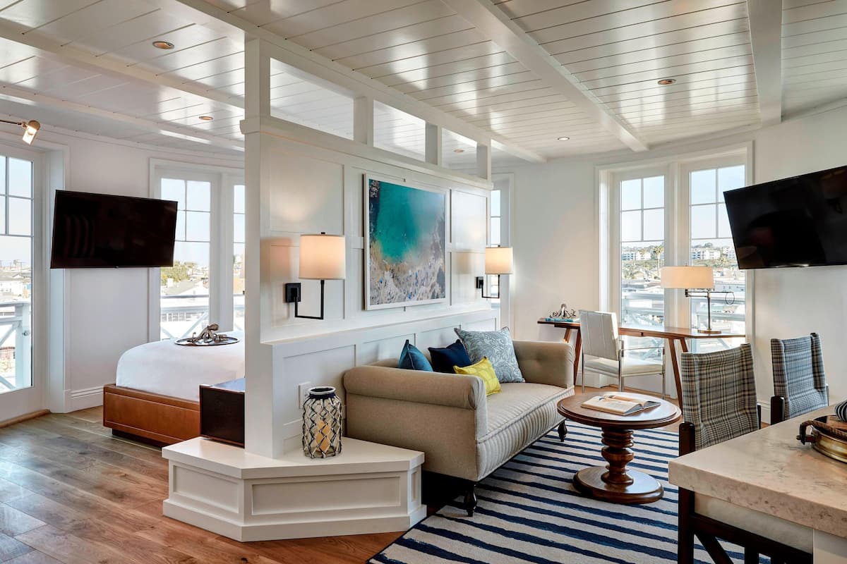 A modern living room with a large bed, a sofa, and a dining area. There are large windows with a view of the city.
