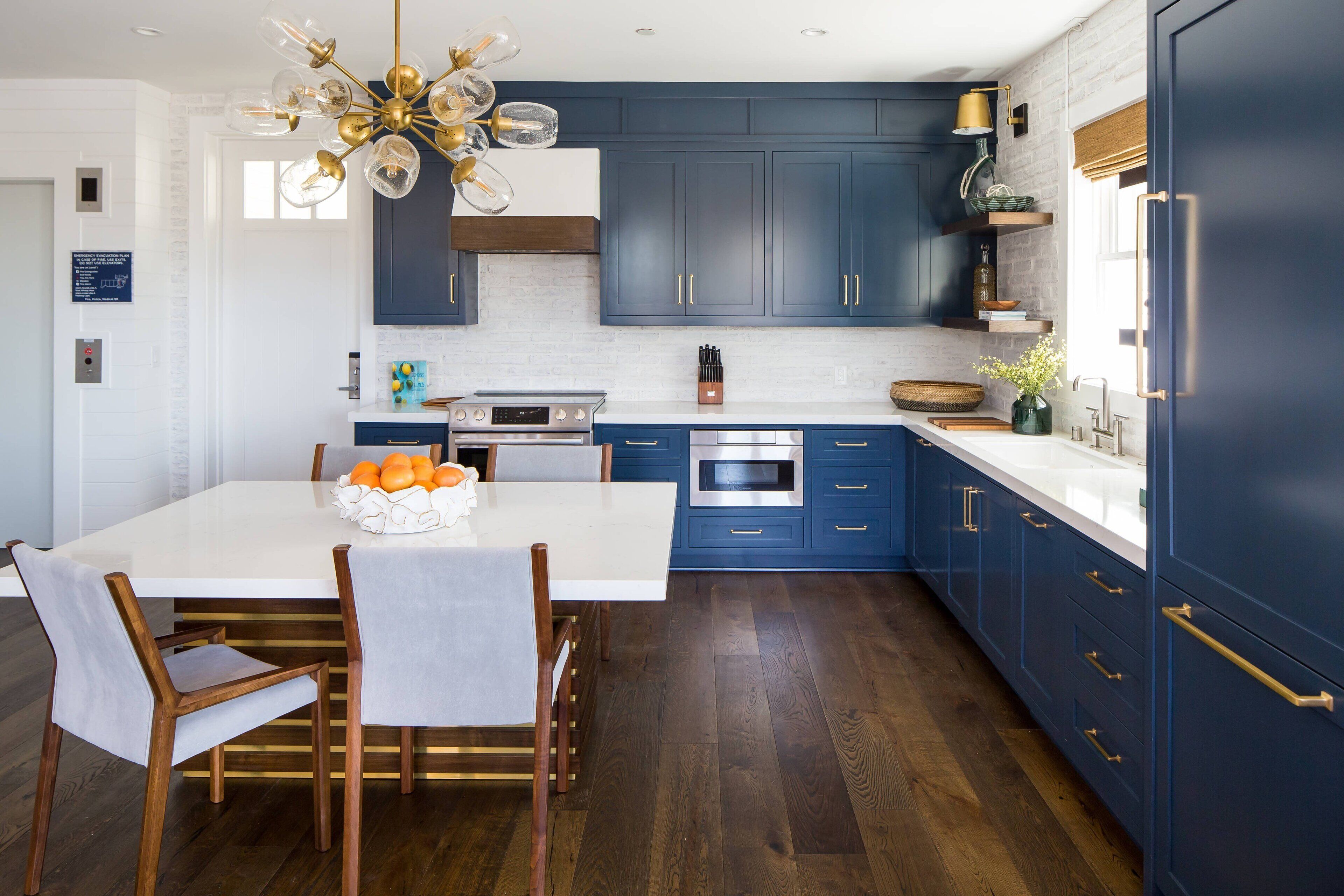 Een moderne keuken met blauwe kastjes, een wit kookeiland en een kroonluchter.