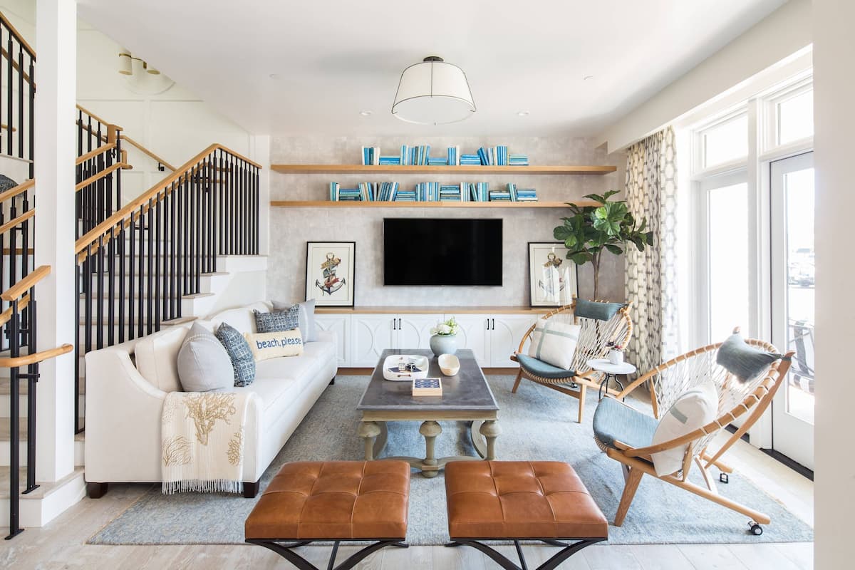 A modern living room with a sofa, coffee table, and chairs, a TV mounted on the wall, and a staircase with wooden railings.