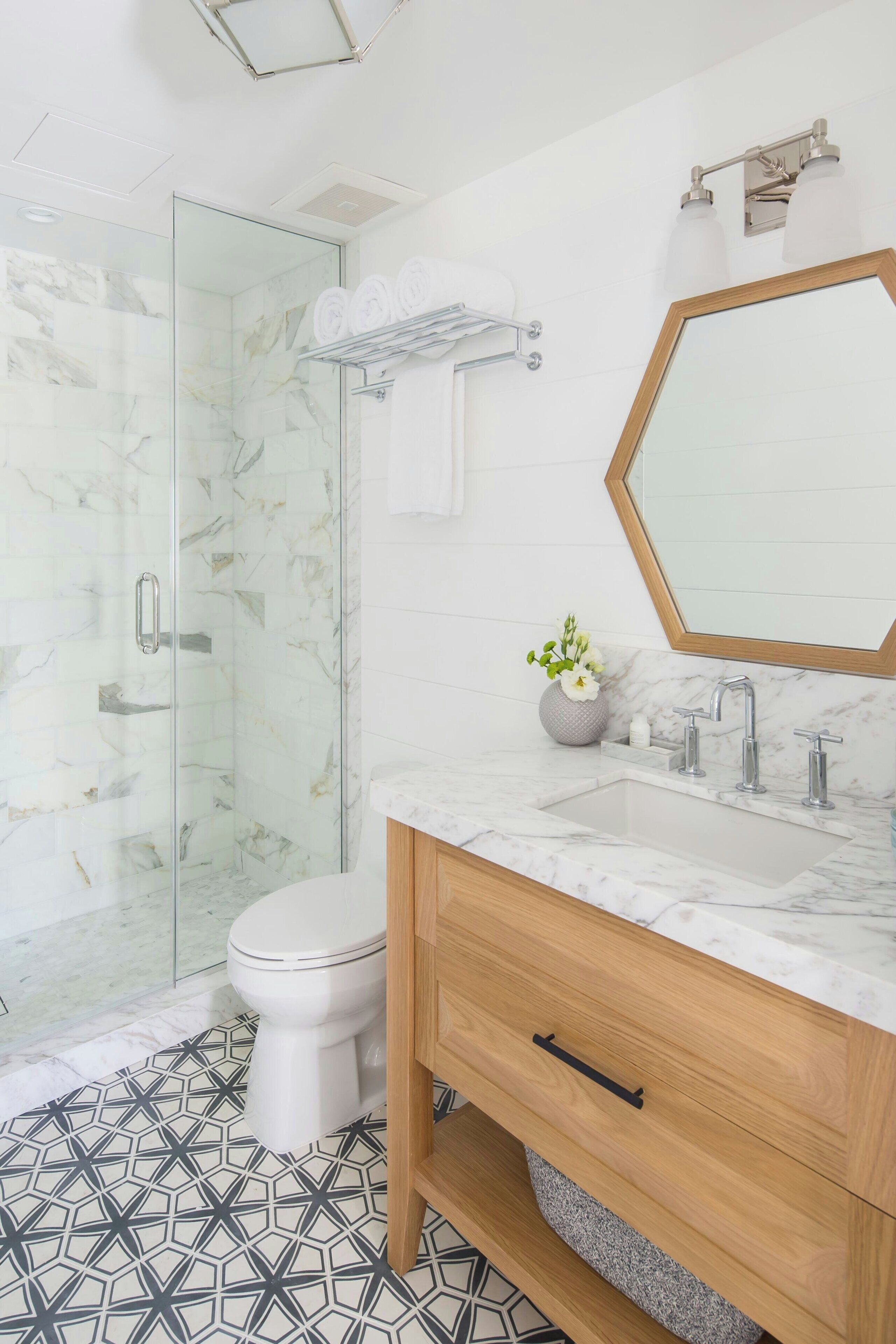 Un baño moderno con ducha envuelta en vidrio, inodoro blanco, lavamanos de mármol y tocador de madera.
