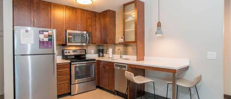 Una cocina moderna con electrodomésticos de acero inoxidable, armarios de madera, un microondas, una cafetera y una zona de bar con dos taburetes.