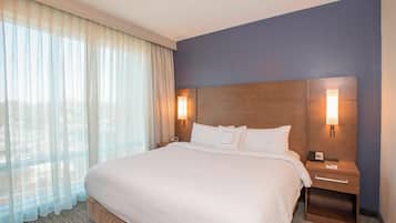 Habitación de hotel con una cama grande, dos mesitas de noche con lámparas, una ventana con cortinas translúcidas y una pared de acento azul oscuro.