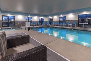 Zona de piscina con sillones de descanso y una pequeña mesa, rodeada de ventanas.