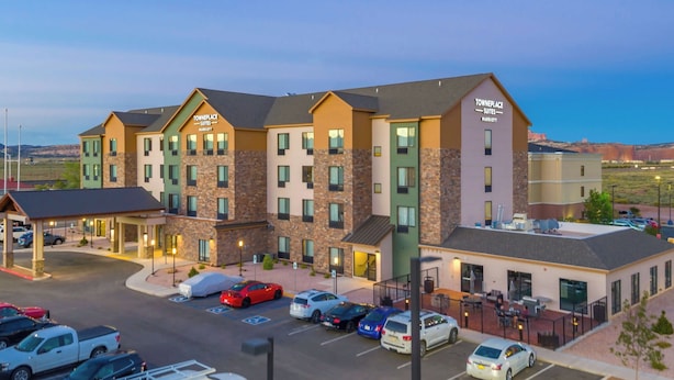 A multi-story hotel with a modern design, featuring a parking lot with several cars and a small outdoor seating area.