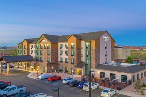A multi-story hotel with a modern design, featuring a parking lot with several cars and a small outdoor seating area. - TownePlace Suites by Marriott Gallup (Gallup)