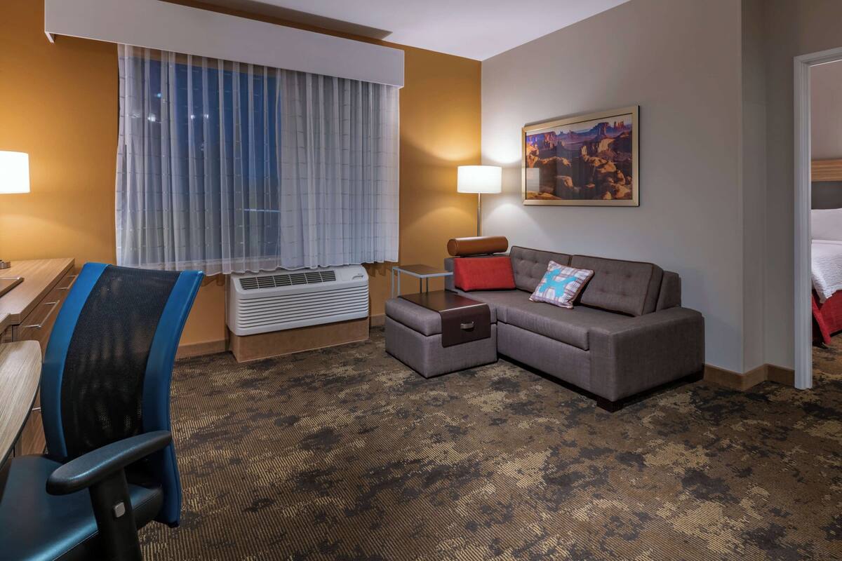 Ett hotellrum med en soffa, en stol, ett skrivbord, en lampa och en tavla på väggen.