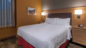 A hotel room with a large bed, wooden headboard, two bedside tables with lamps, a red carpet, and a framed picture on the wall.