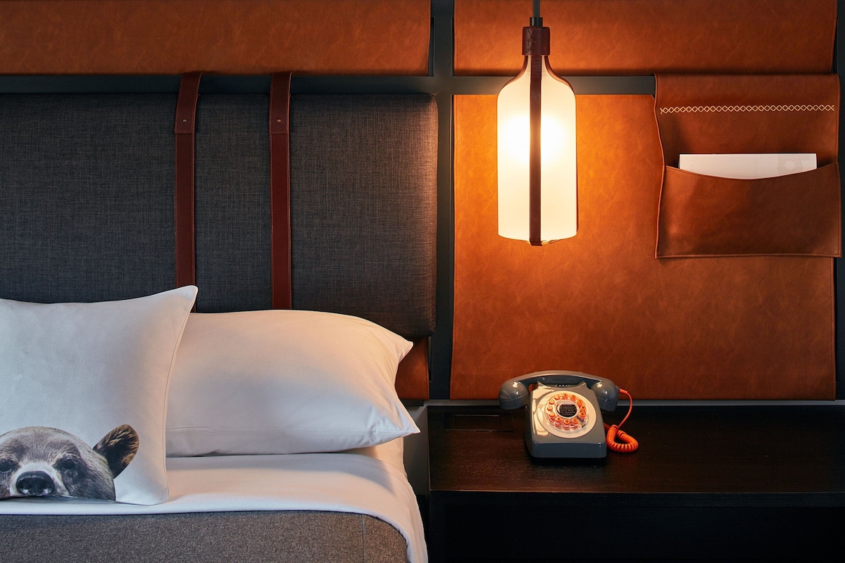 Une chambre d’hôtel équipée d’un lit, d’une table de chevet, d’un téléphone et d’un luminaire fixé au mur.